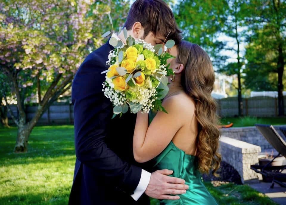 A garden kiss behind a bright bouquet