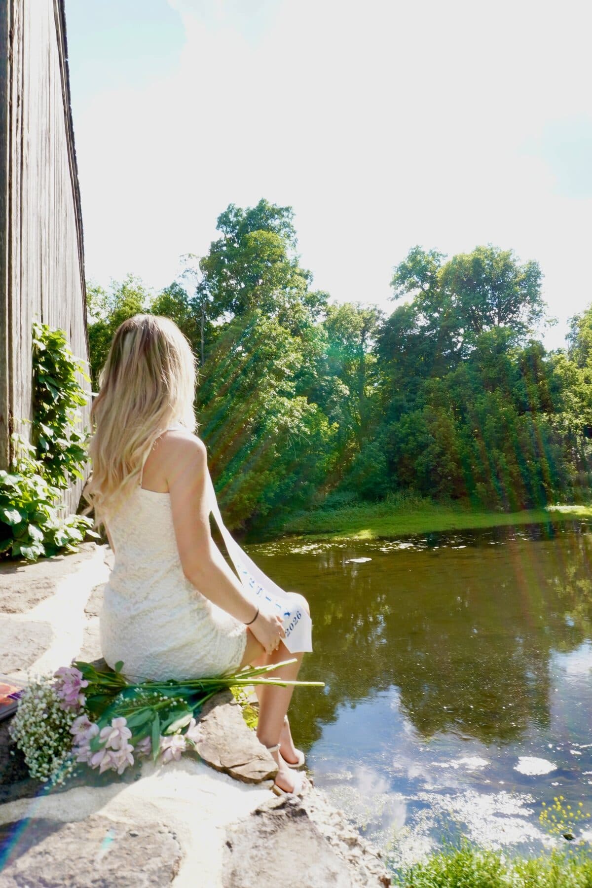 Seated beside a quiet pond in a white dress